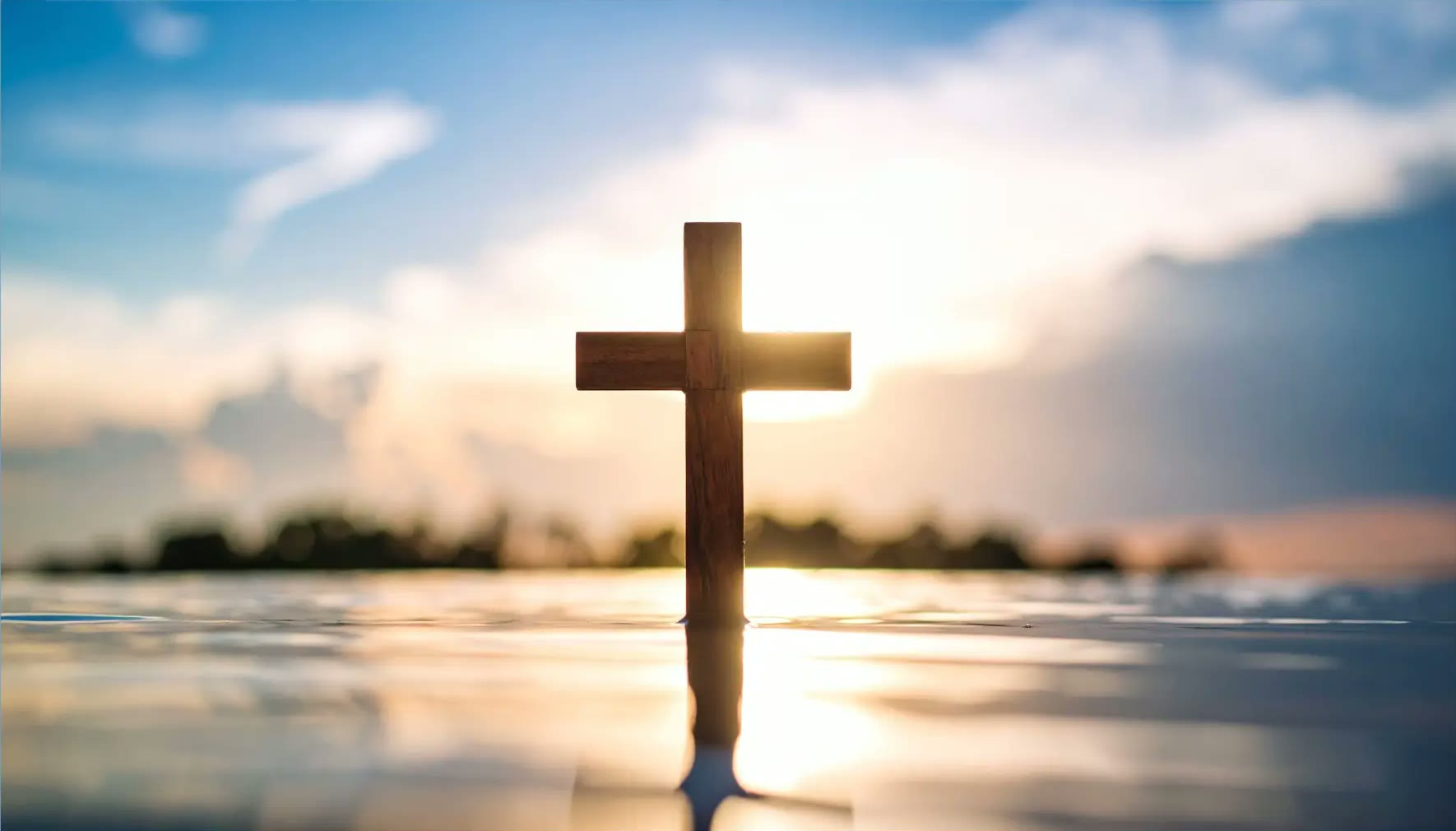 Wooden cross at sunrise over still water